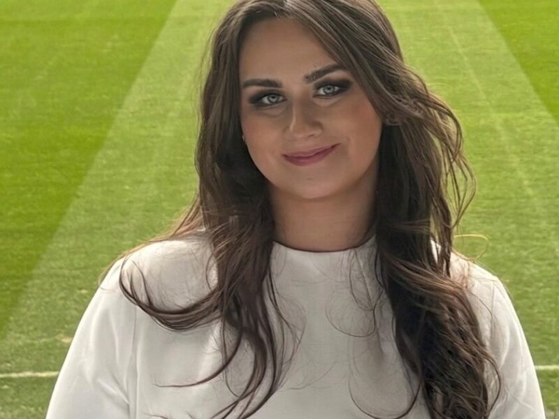 Tiff standing in front of a football pitch smiling.
