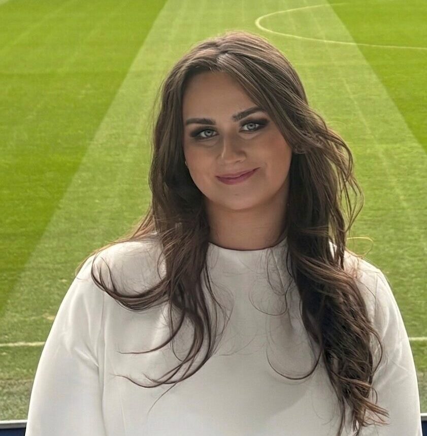 Tiff standing in front of a football pitch smiling.
