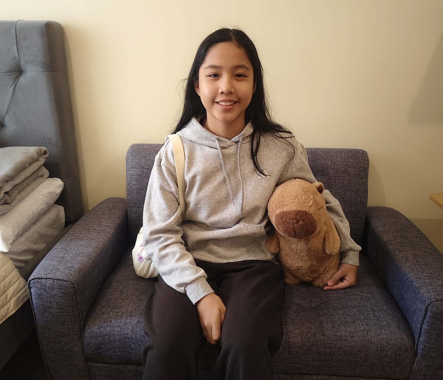 A young teenager sits on a chair and smiles at the camera.