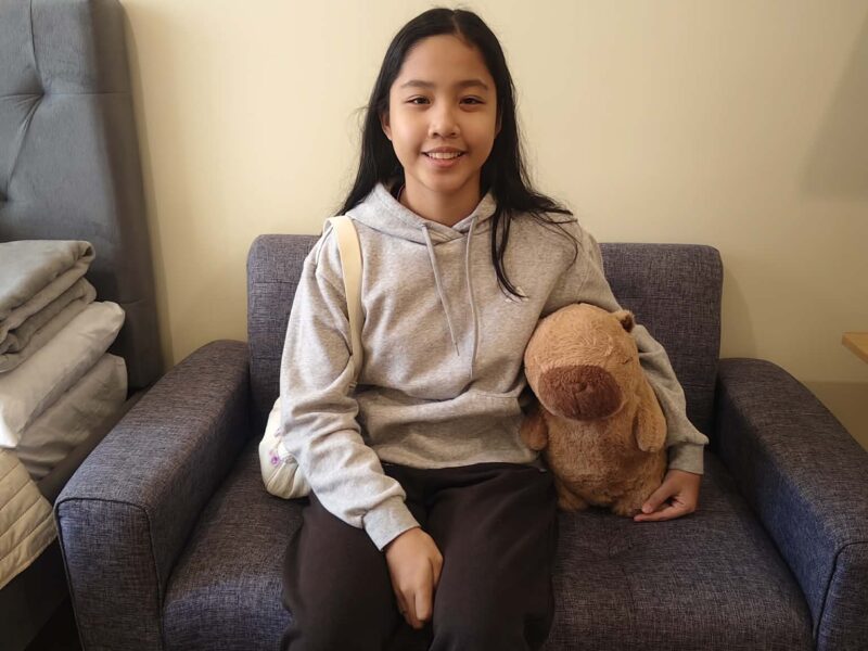 A young teenager sits on a chair and smiles at the camera.