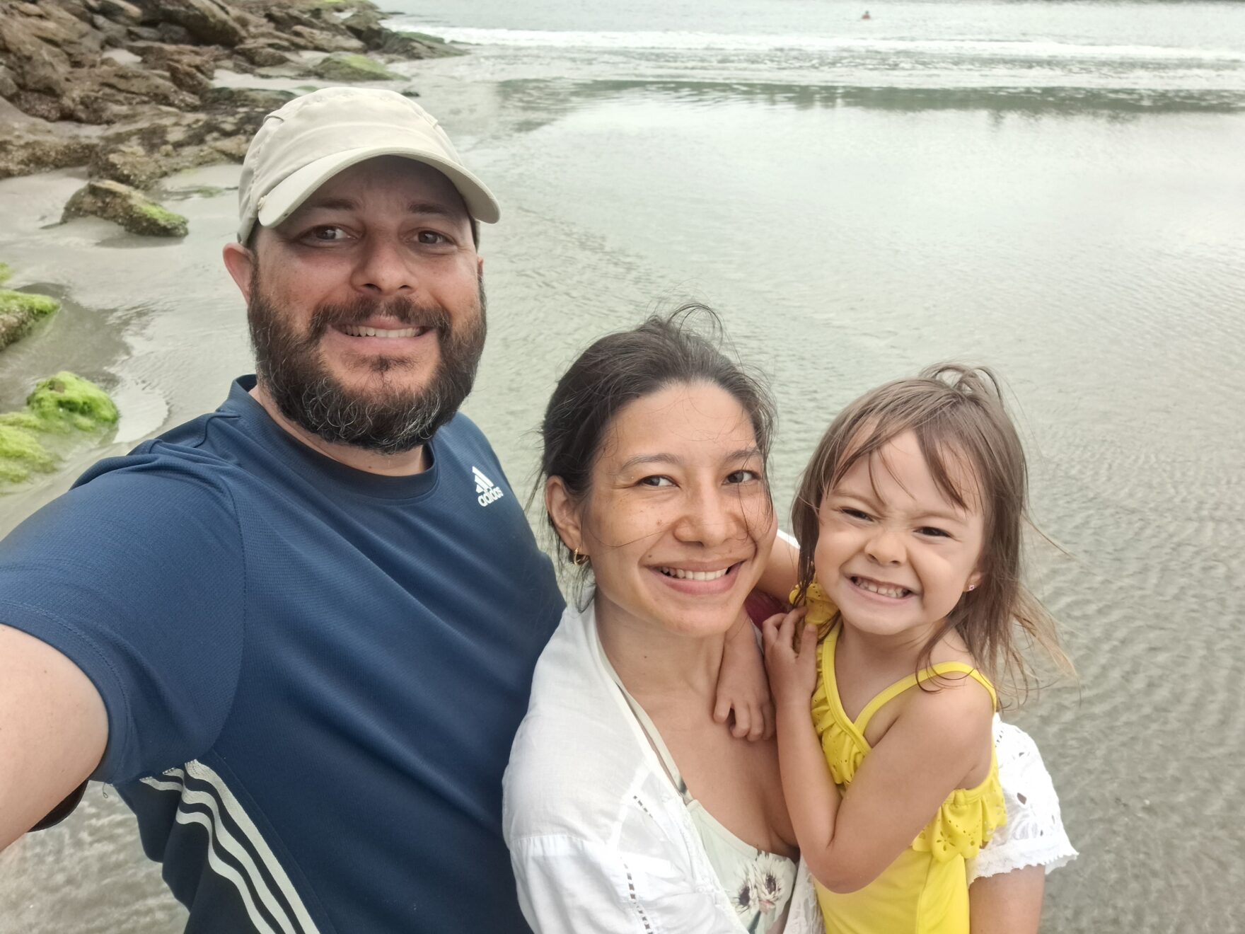 Two parents and a child stand on a beach smiling at the camera