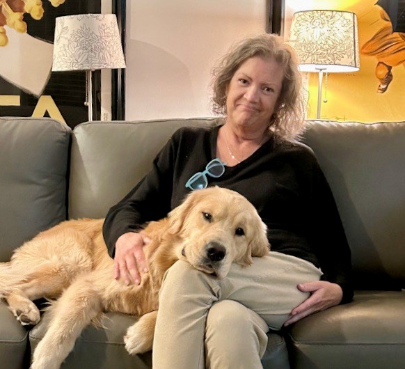 A lady sits with a dog on a sofa.