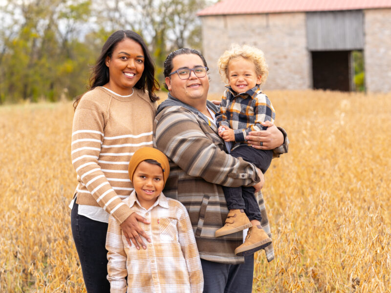 Parents and two young children stand together smiling at the camera.