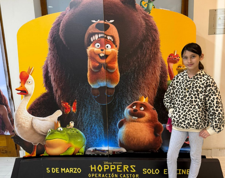 A young girl stands in front of a movie poster.