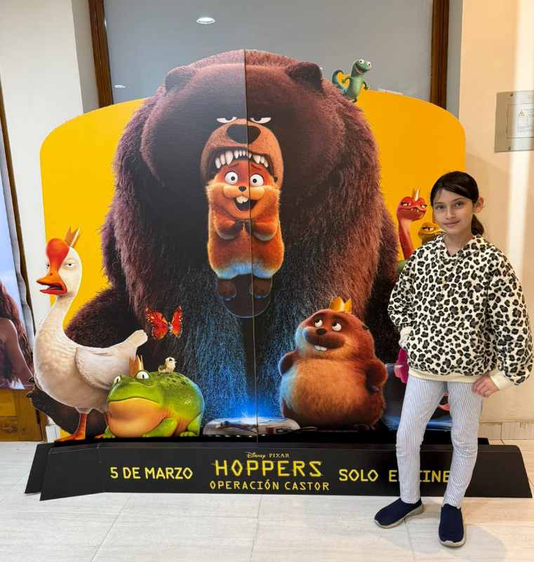 A young girl stands in front of a movie poster.